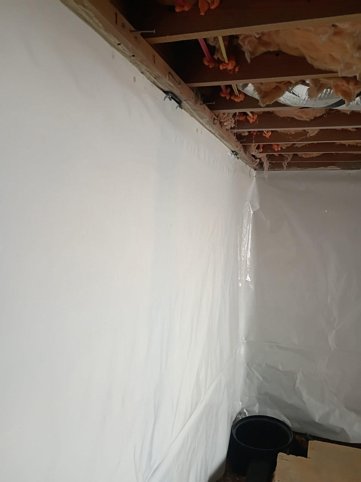 Finished interior basement wall with a white vapor barrier covering the block — the wall-treatment side of a completed Basement Medic waterproofing job